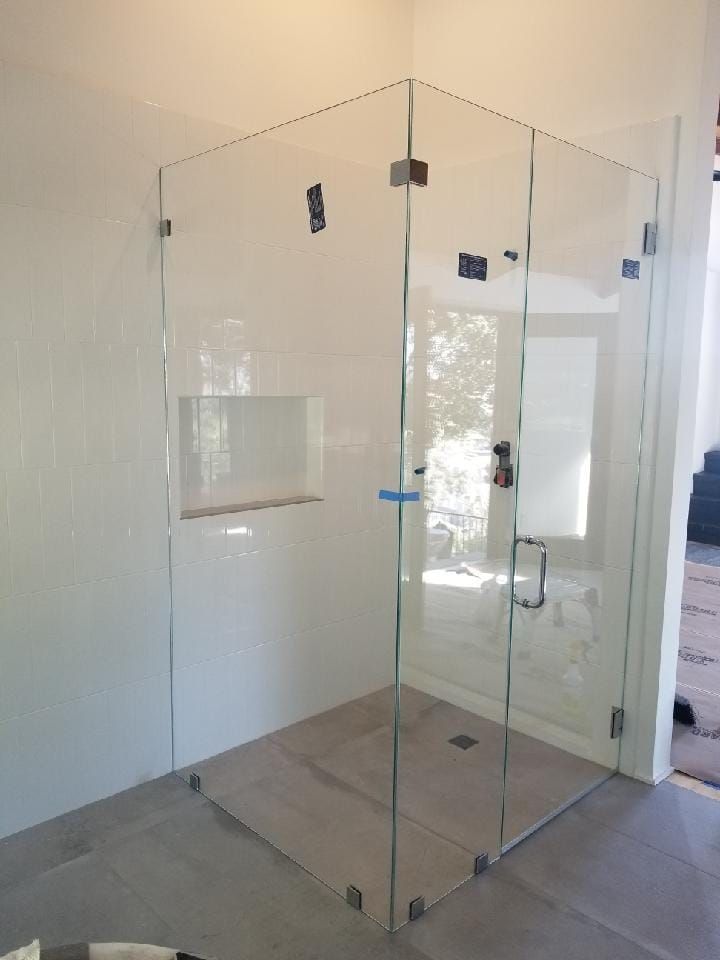 Glass shower enclosure in a bathroom. White tile walls, gray floor, with a recessed shelf.