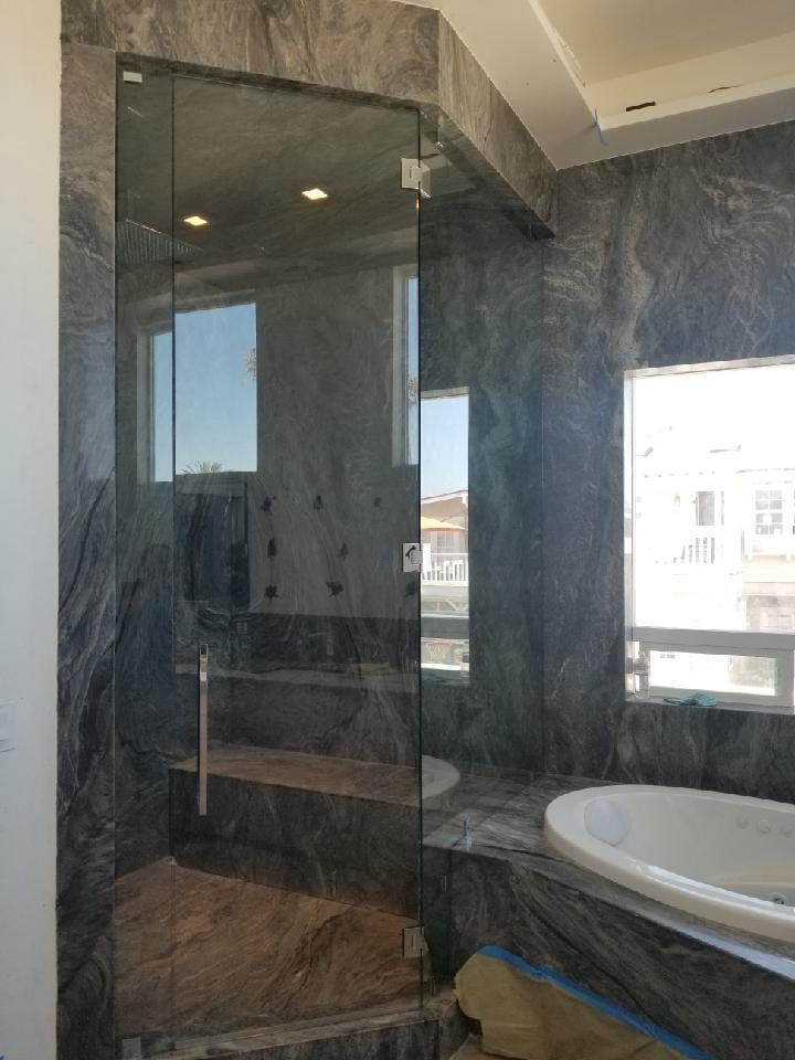Glass shower enclosure in a marble-tiled bathroom.  Includes a door, a shower head, and a tub.