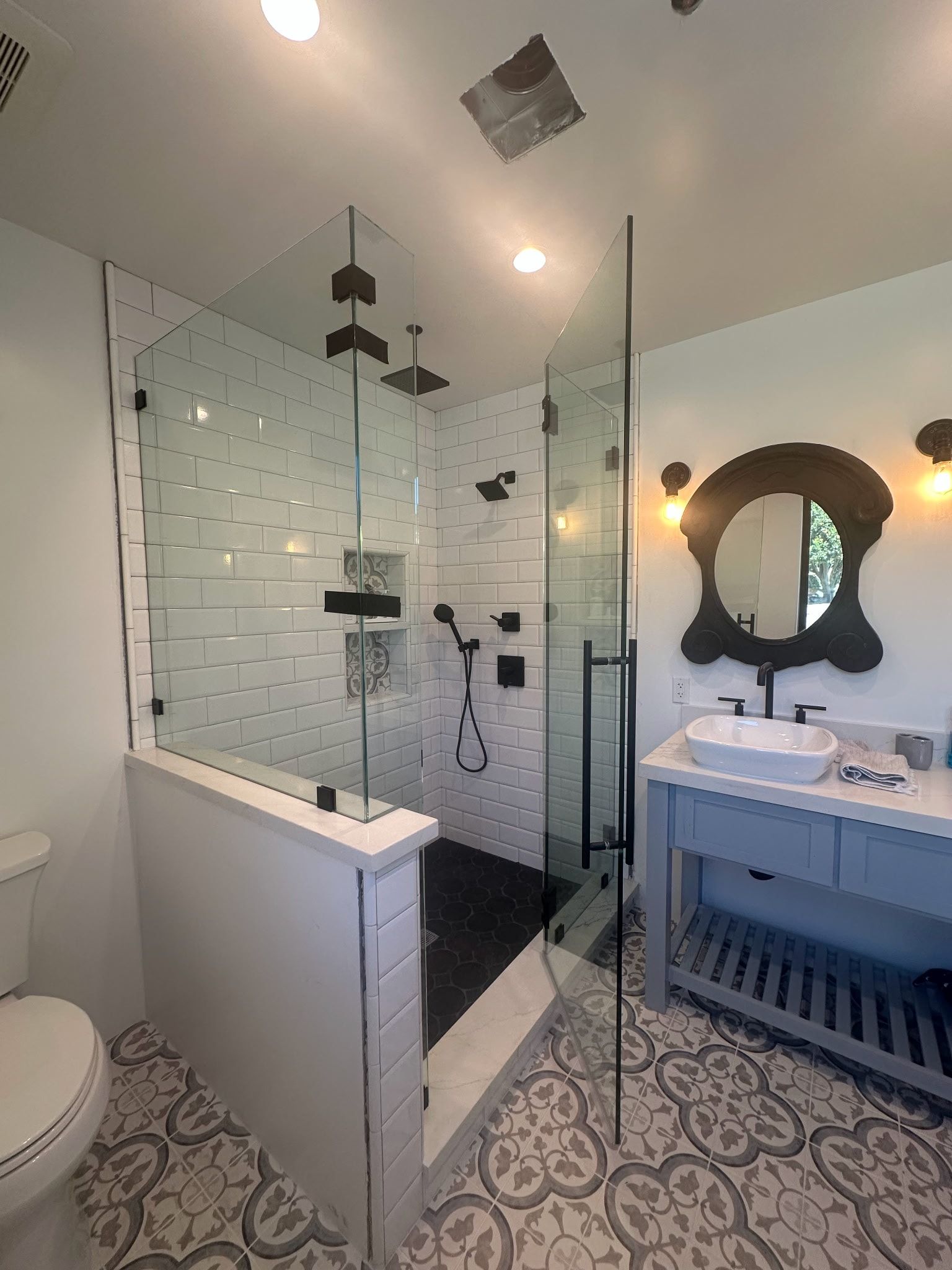 Modern bathroom with glass shower, white subway tile, black fixtures, patterned floor, and a blue vanity.