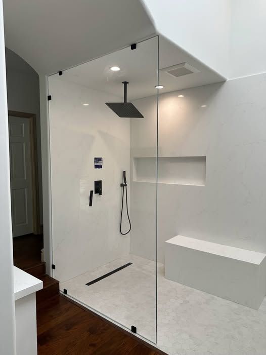Modern, white-walled shower with glass enclosure, black fixtures, and built-in bench.