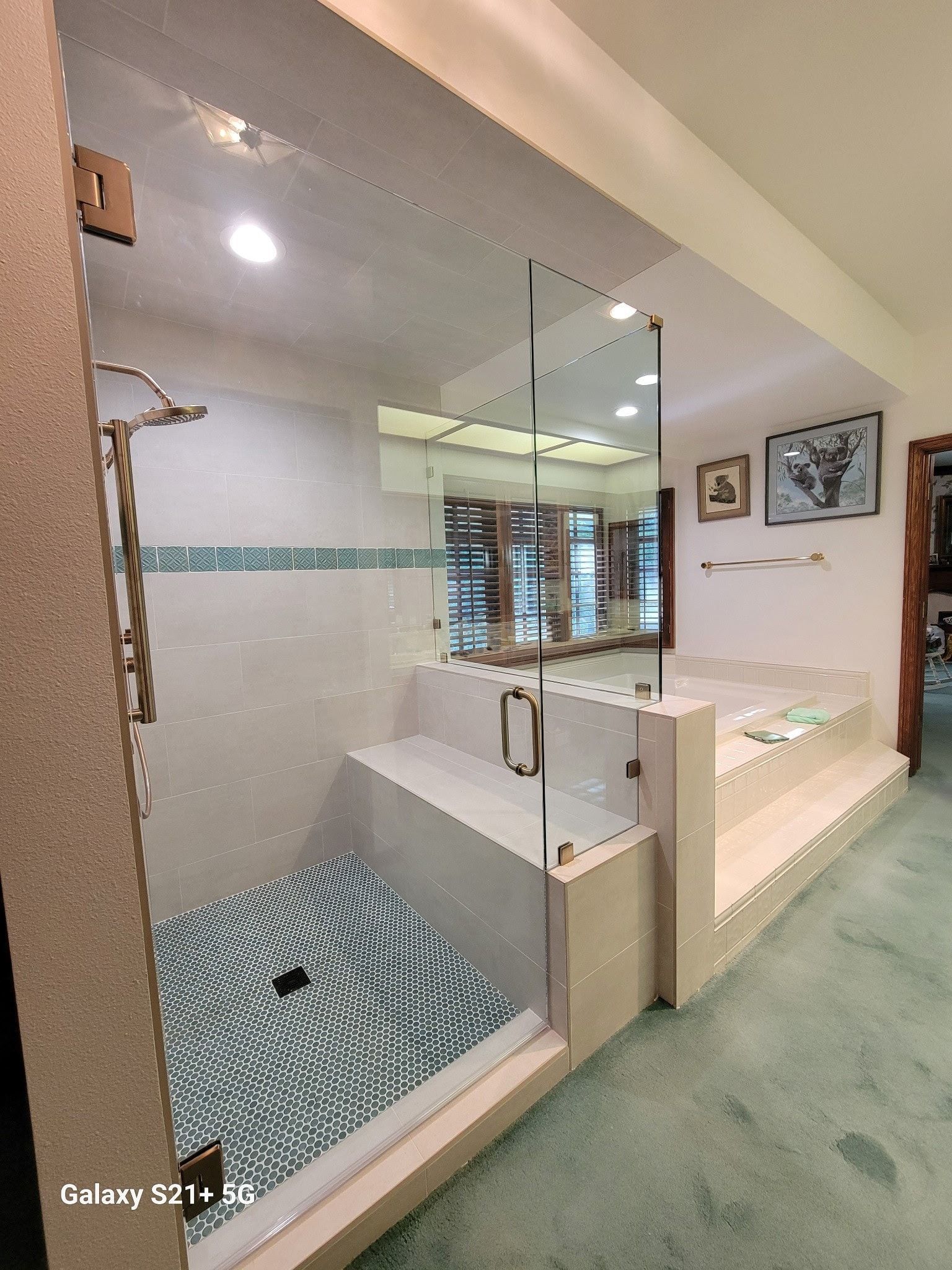 Bathroom with glass shower, tiled floor, step-up tub, art, and green carpet.