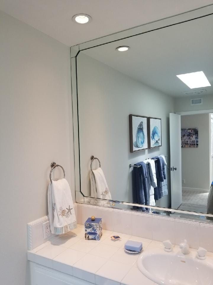 Bathroom with large mirror, white countertop, two recessed lights, artwork, and towels.