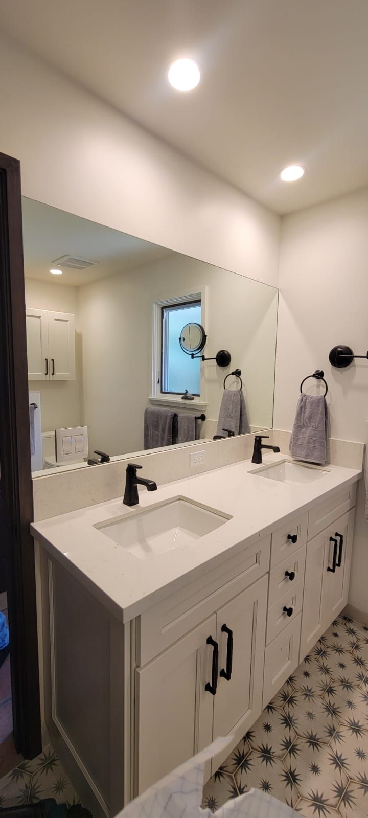 Bathroom vanity with white cabinets, black hardware, black faucets, and large mirror.