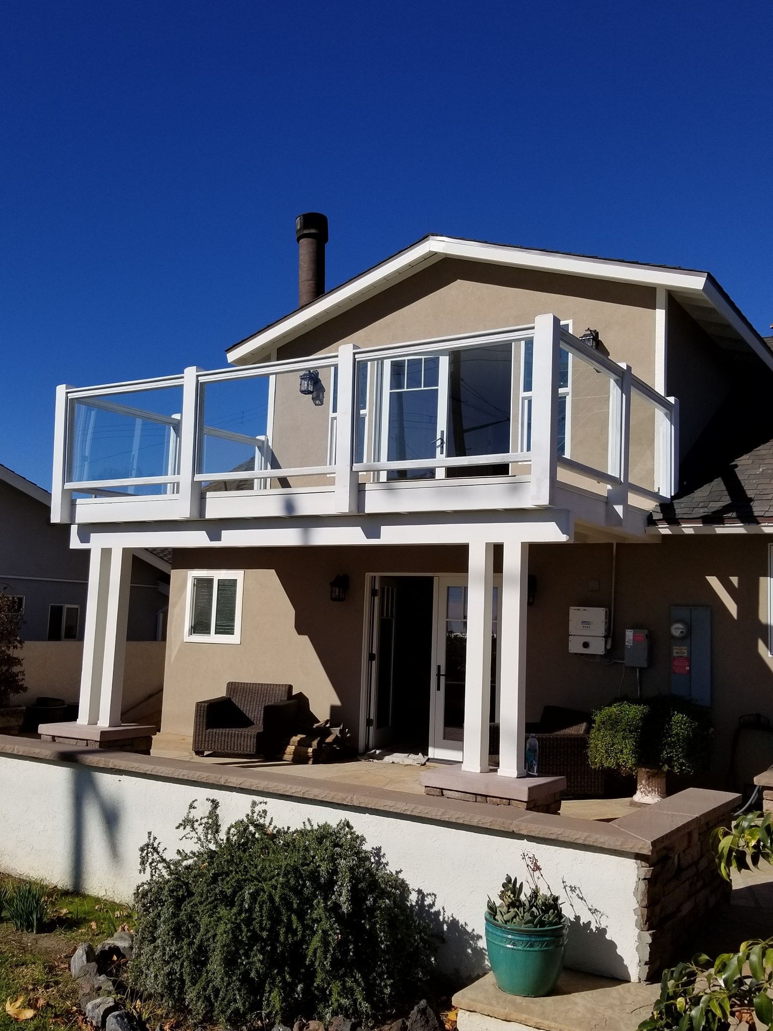 Two-story beige house with white railing balcony, blue sky background.