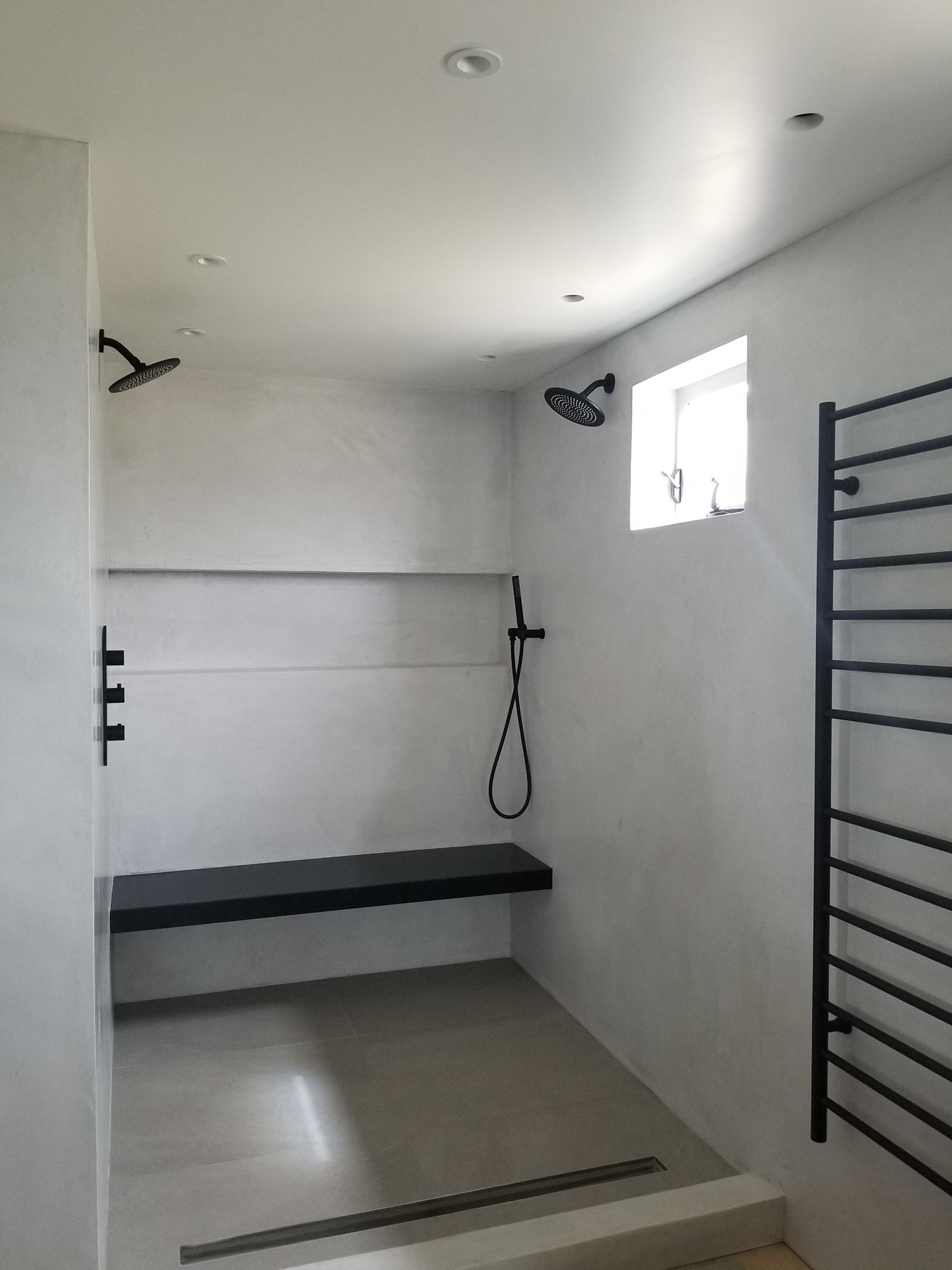 Modern, accessible shower with black fixtures, a bench, and a heated towel rack.