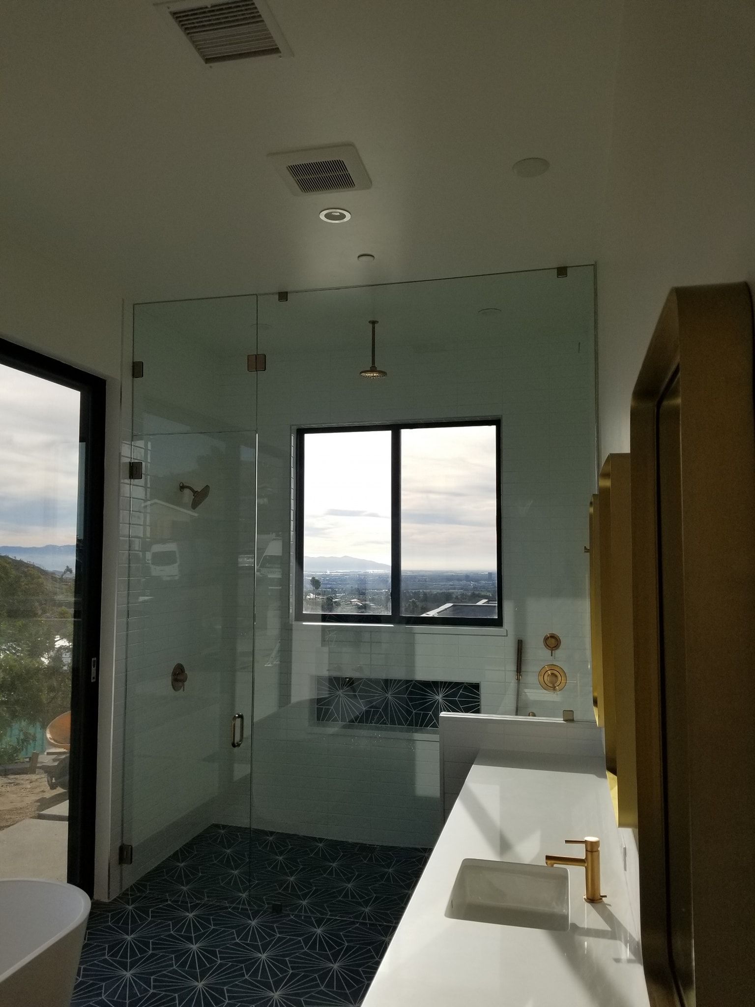 Modern bathroom with large glass shower, window with mountain view, and white vanity.