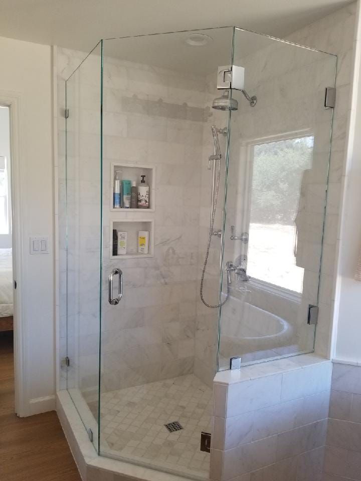 Glass-enclosed shower with white tiled walls, a window, and built-in shelves.