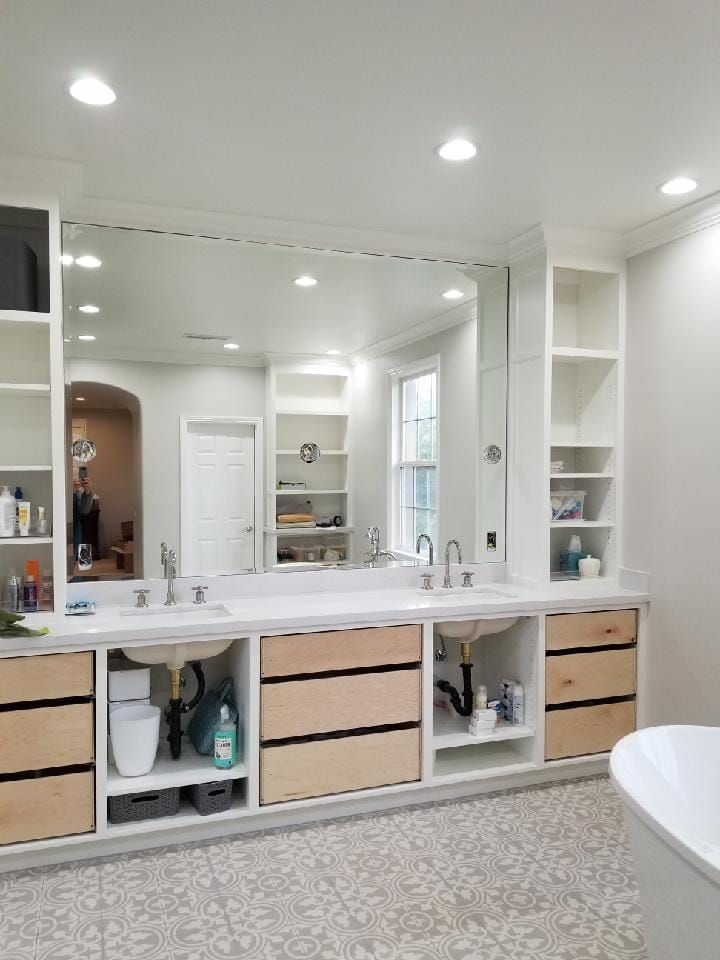 Spacious white bathroom with large mirror, double sinks, light wood drawers, and open shelving.