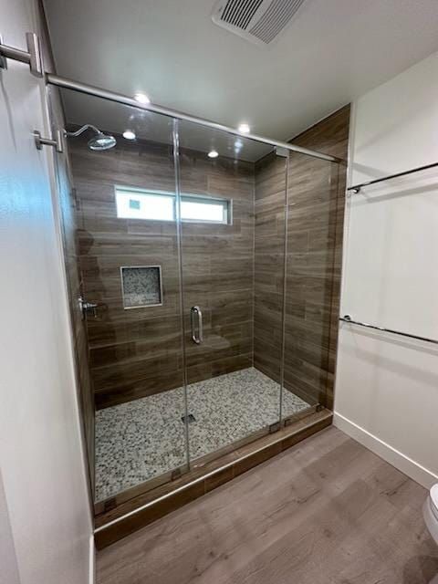 Modern shower with glass doors, stone floor, wood-look tile walls, and stainless steel fixtures.