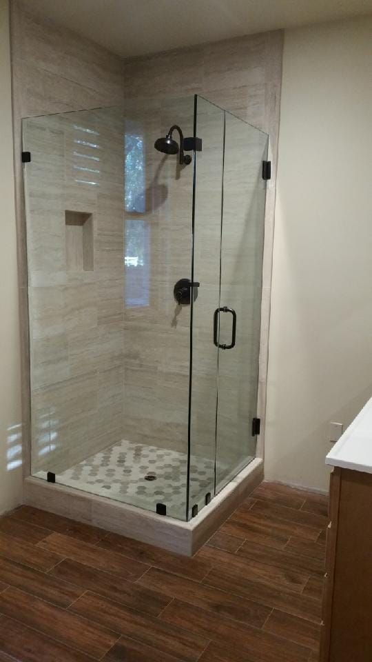 Glass shower enclosure with black fixtures and stone tile floor.