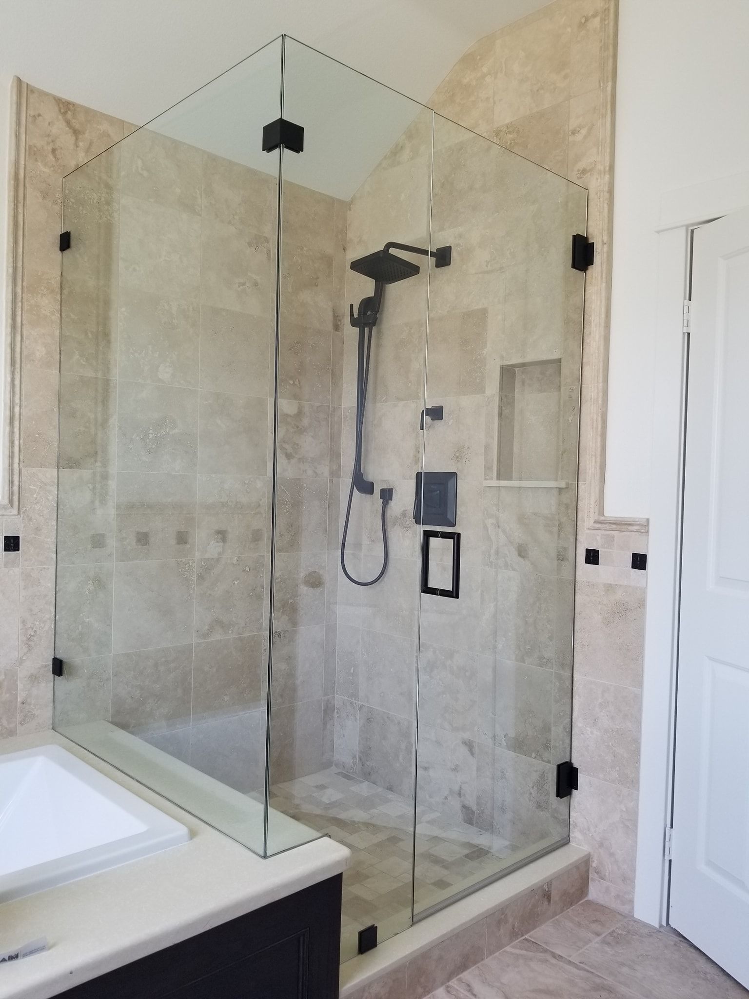 Glass shower enclosure with black fixtures in a tiled bathroom.