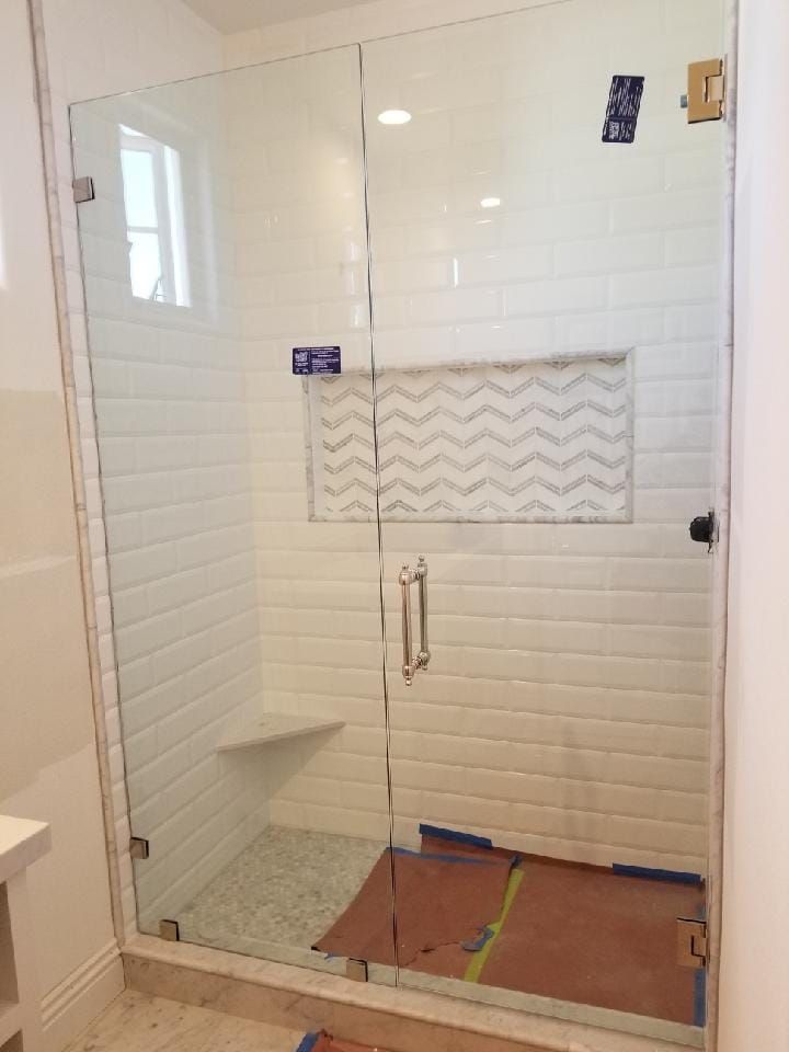 Glass shower enclosure with white tile walls, a built-in seat, and open doors.