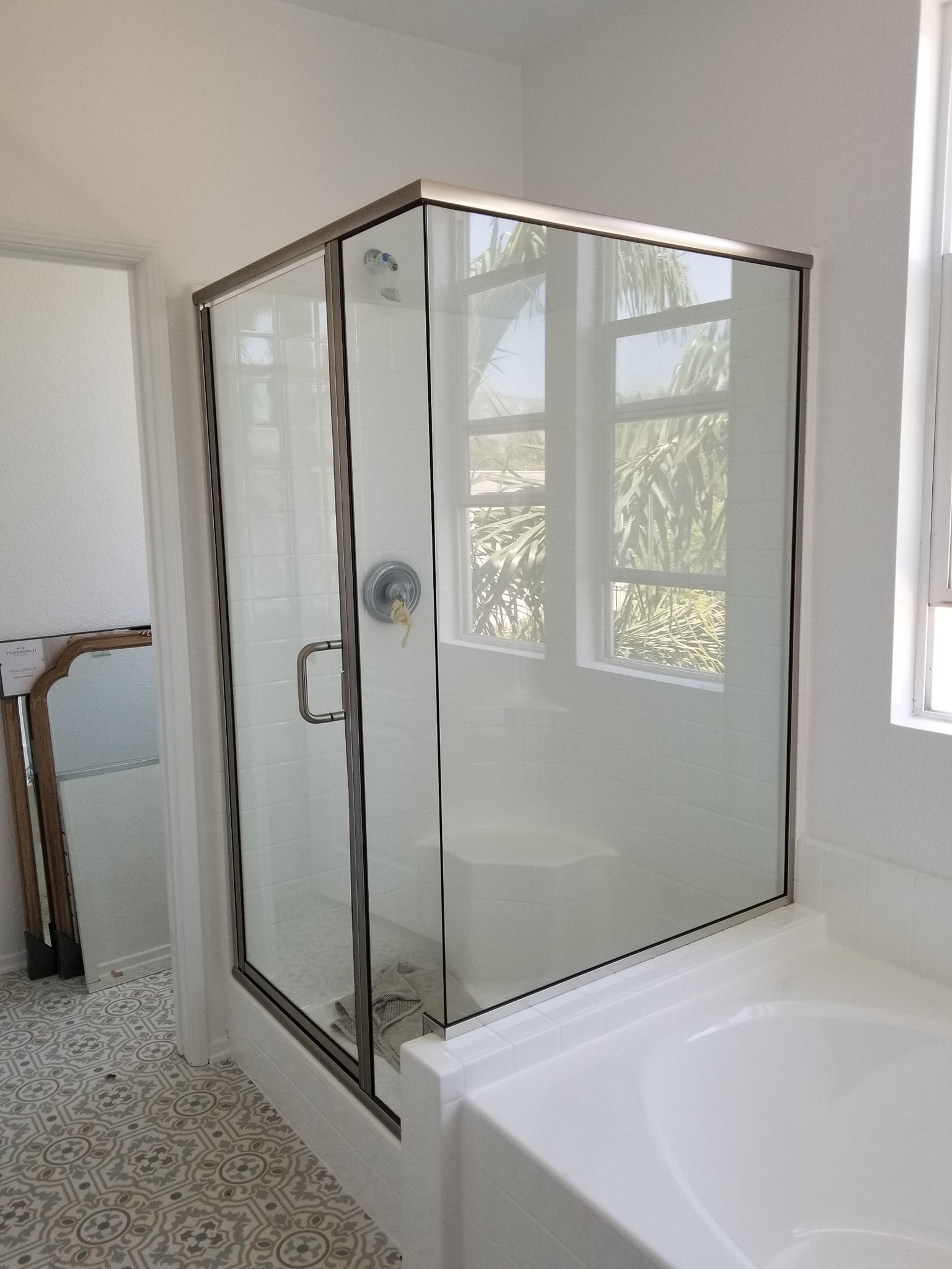 Shower with glass doors and silver trim, adjacent to a bathtub, with a tiled floor.