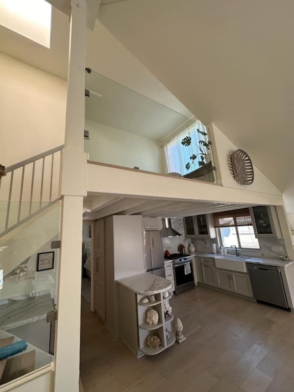Interior view of a modern kitchen with a loft, light wood floors, and a white and gray color scheme.