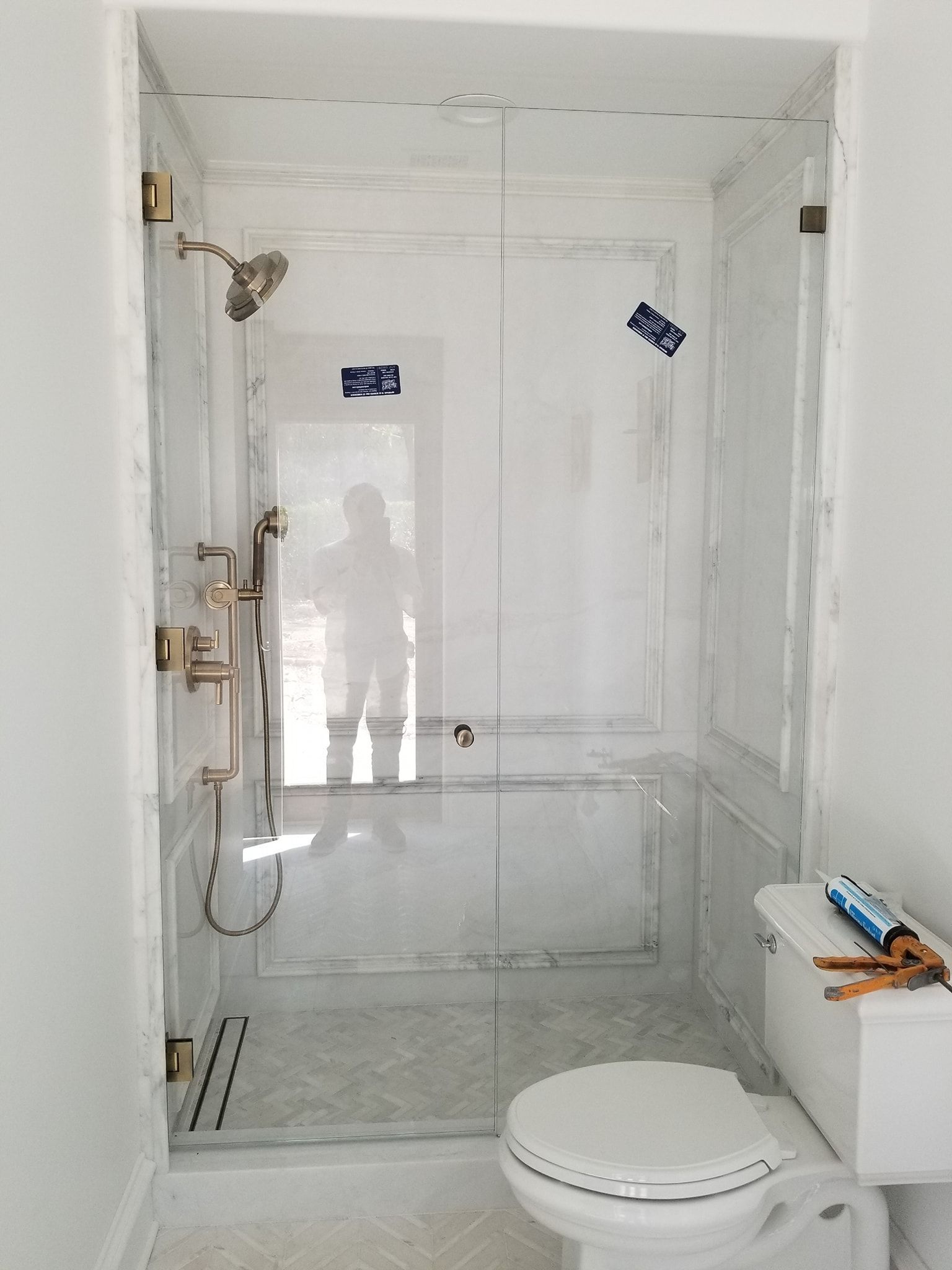 Glass shower enclosure in a white bathroom, with gold fixtures and a toilet on the right.
