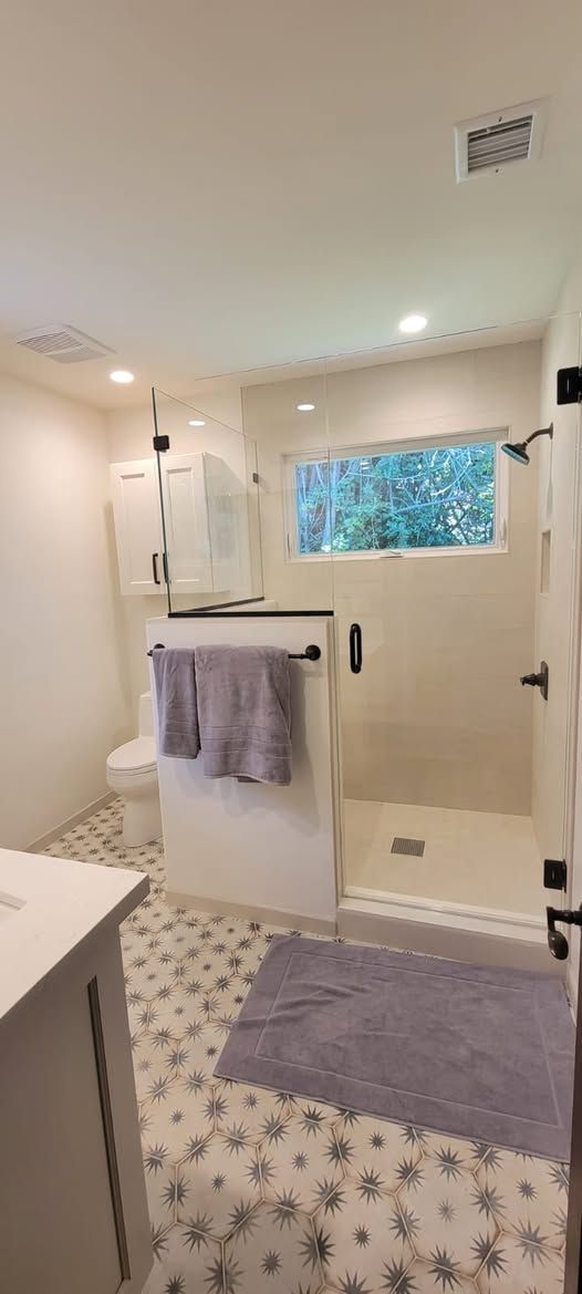 Modern bathroom with a shower, toilet, and patterned tile flooring.