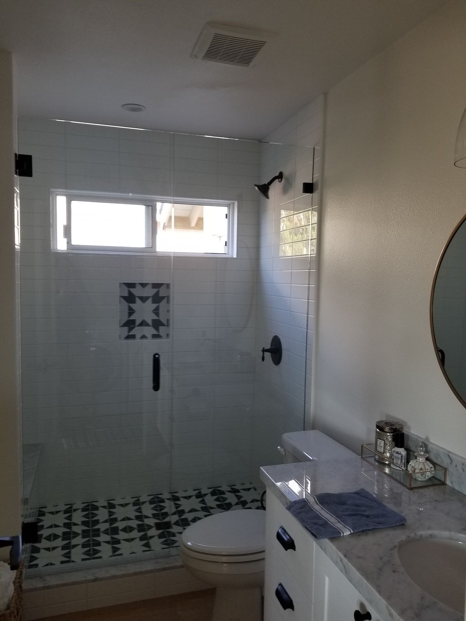 Modern bathroom with glass shower, white and blue tile, toilet, and vanity.
