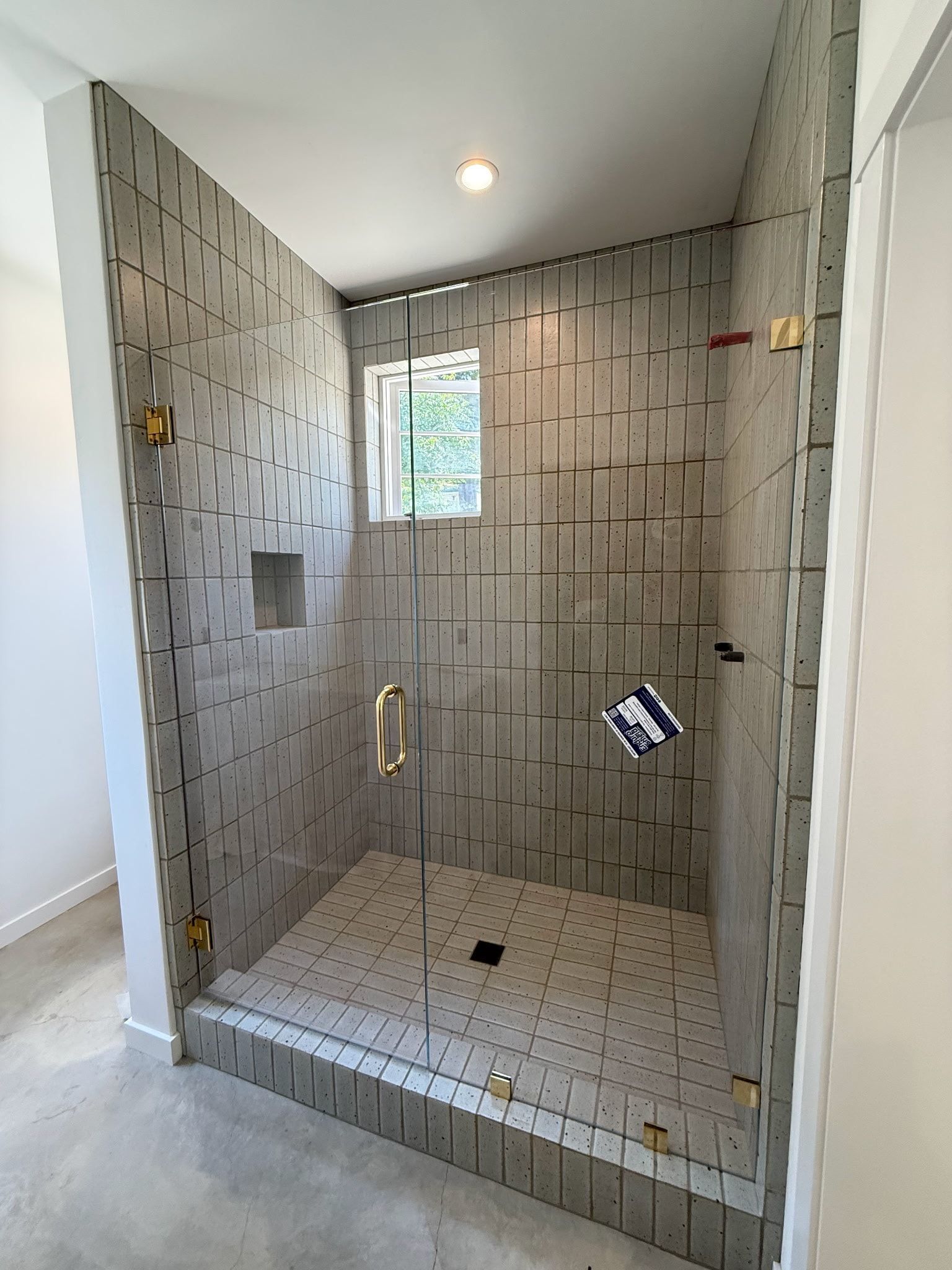 Modern shower with gray patterned tile walls, glass door, and gold fixtures.