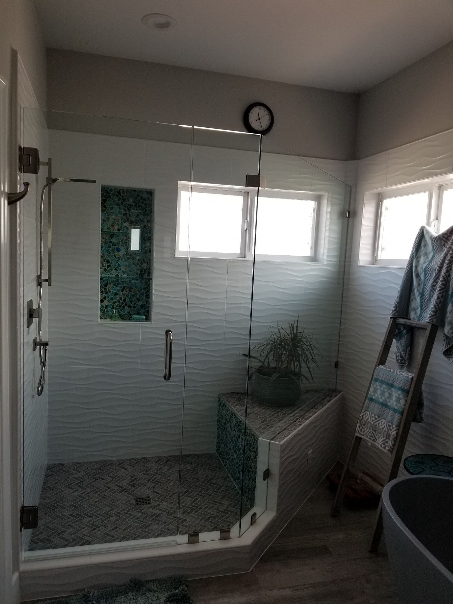 Modern bathroom with glass shower, patterned tiles, small windows, and ladder with towels.