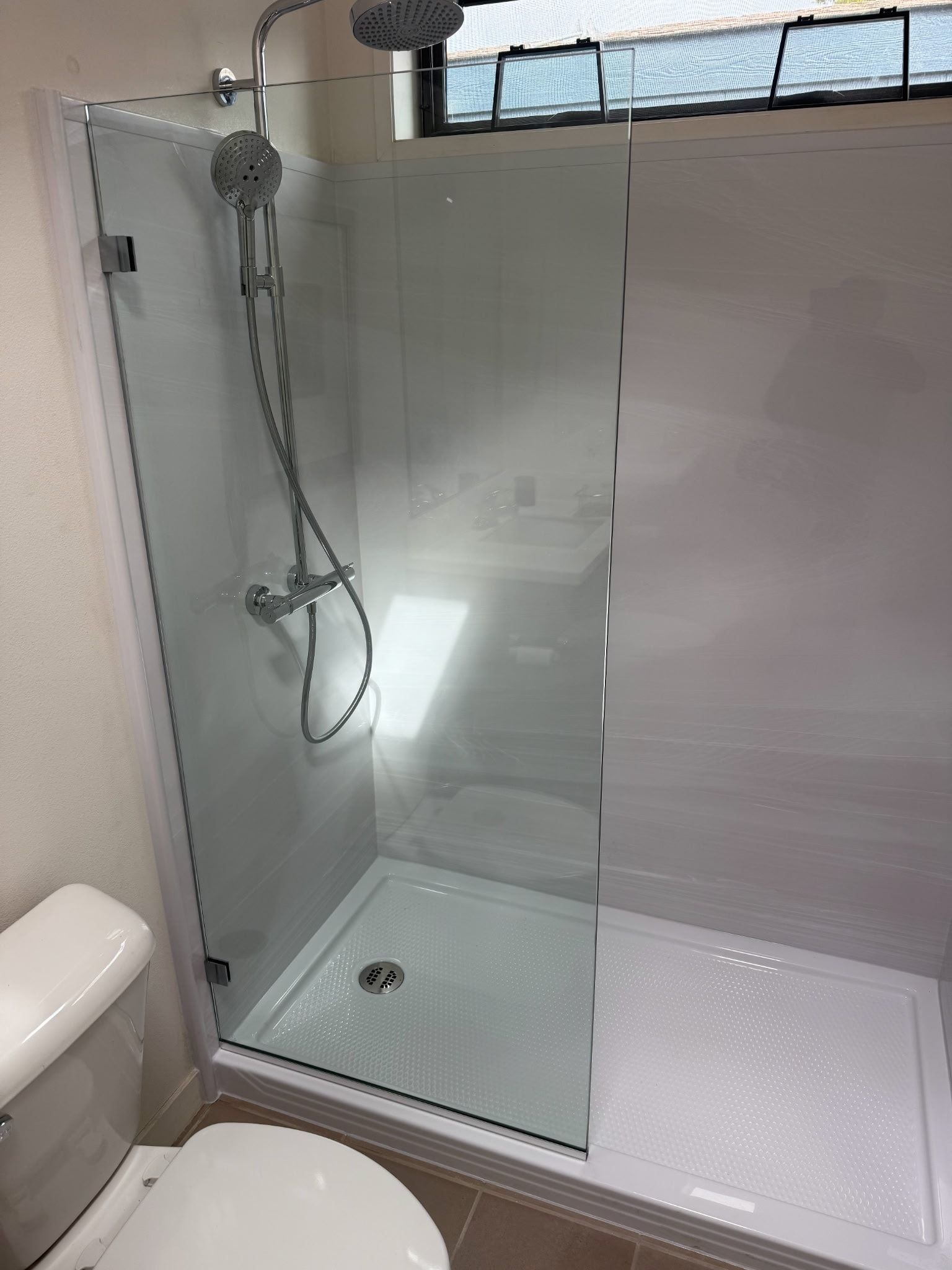 Shower stall with glass doors next to a toilet. White fixtures and shower base.