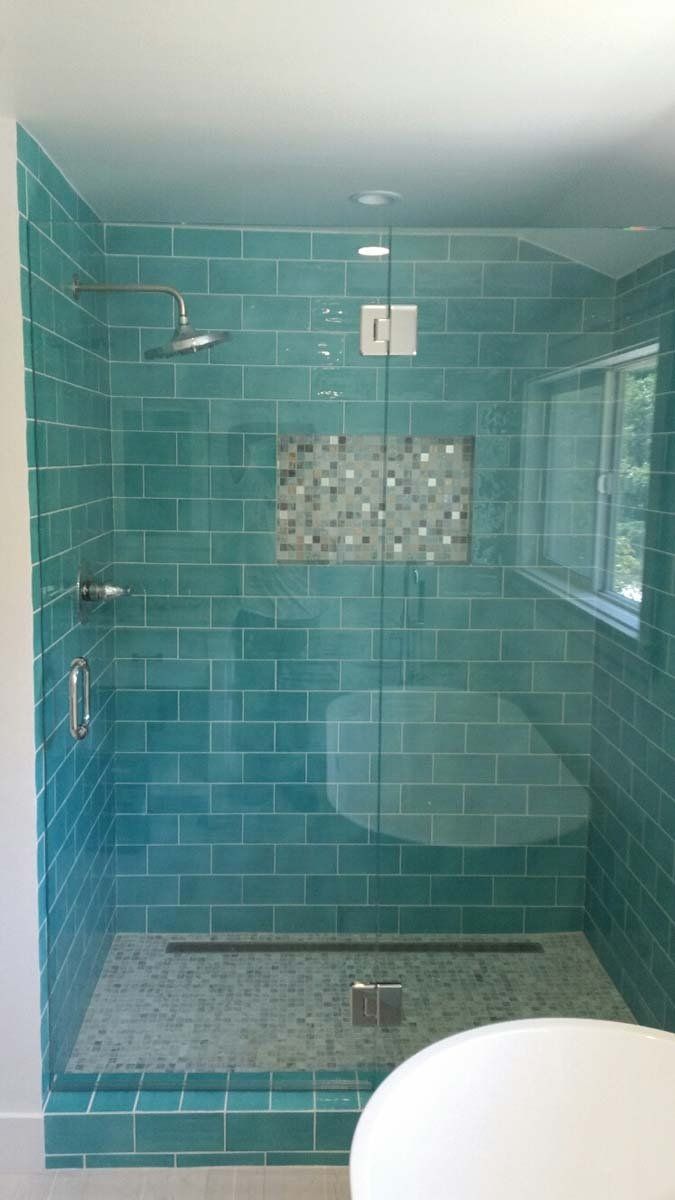 Teal tiled shower with glass door, mosaic niche, and small window.