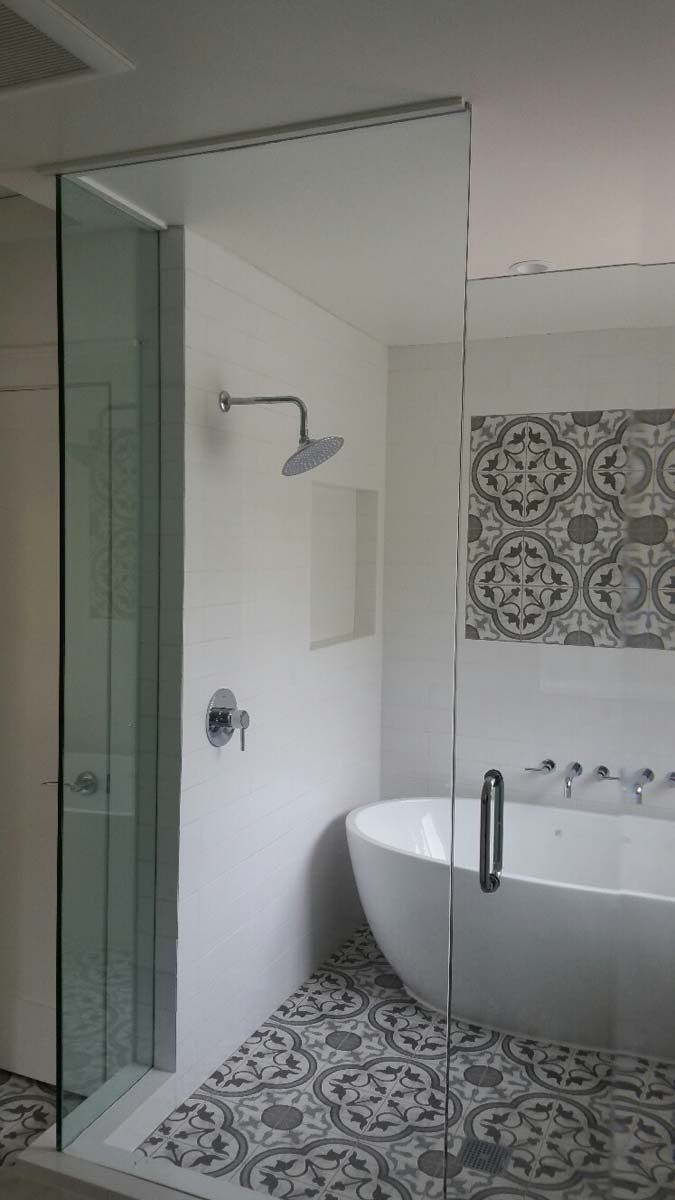 Bathroom with glass shower, soaking tub, patterned floor, and decorative tiled wall.