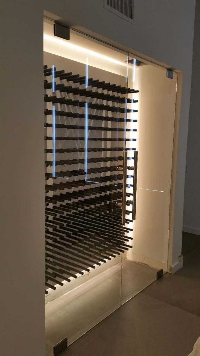 Glass-door wine cellar, backlit with rows of wine bottles on shelves, built into a wall.