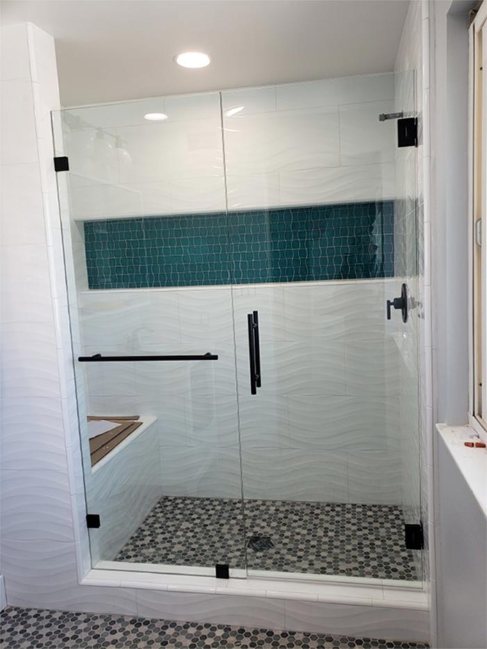 Glass shower with black hardware, teal tile accent, pebble floor.