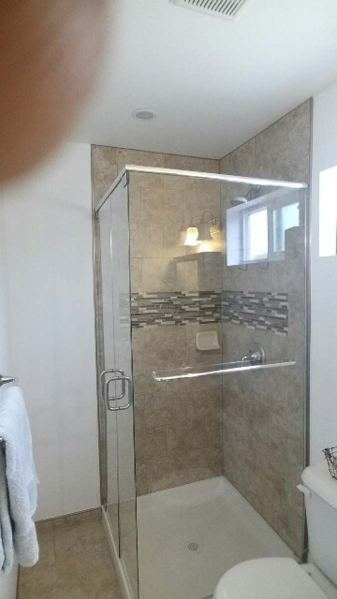 Shower with glass door, tan tile, and white toilet in bathroom.