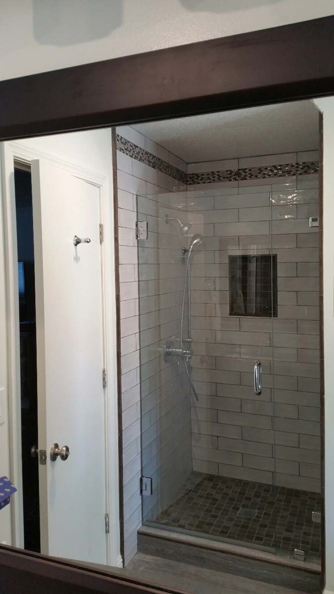 Bathroom with a glass shower, white brick tiles, and dark floor, next to a white door.