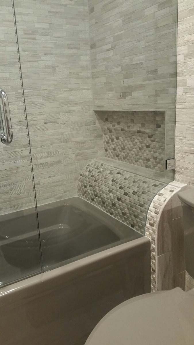 Bathroom with stone tile walls, a tub, and a recessed shelf. Glass shower door on the left.