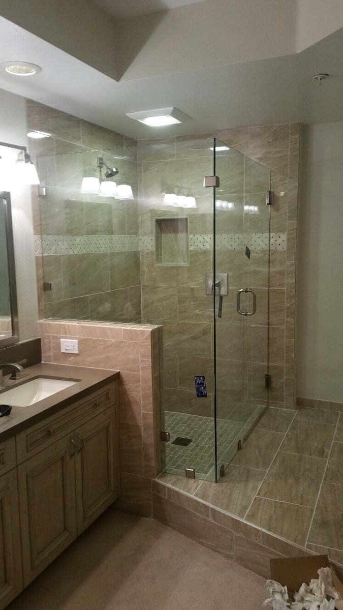 Modern bathroom with glass shower enclosure, tan tile walls, and vanity.