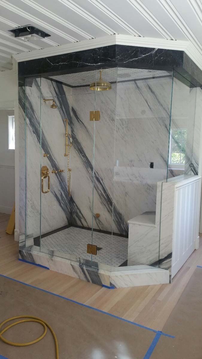 Shower with white and black marble walls, gold fixtures, and glass doors; under construction.