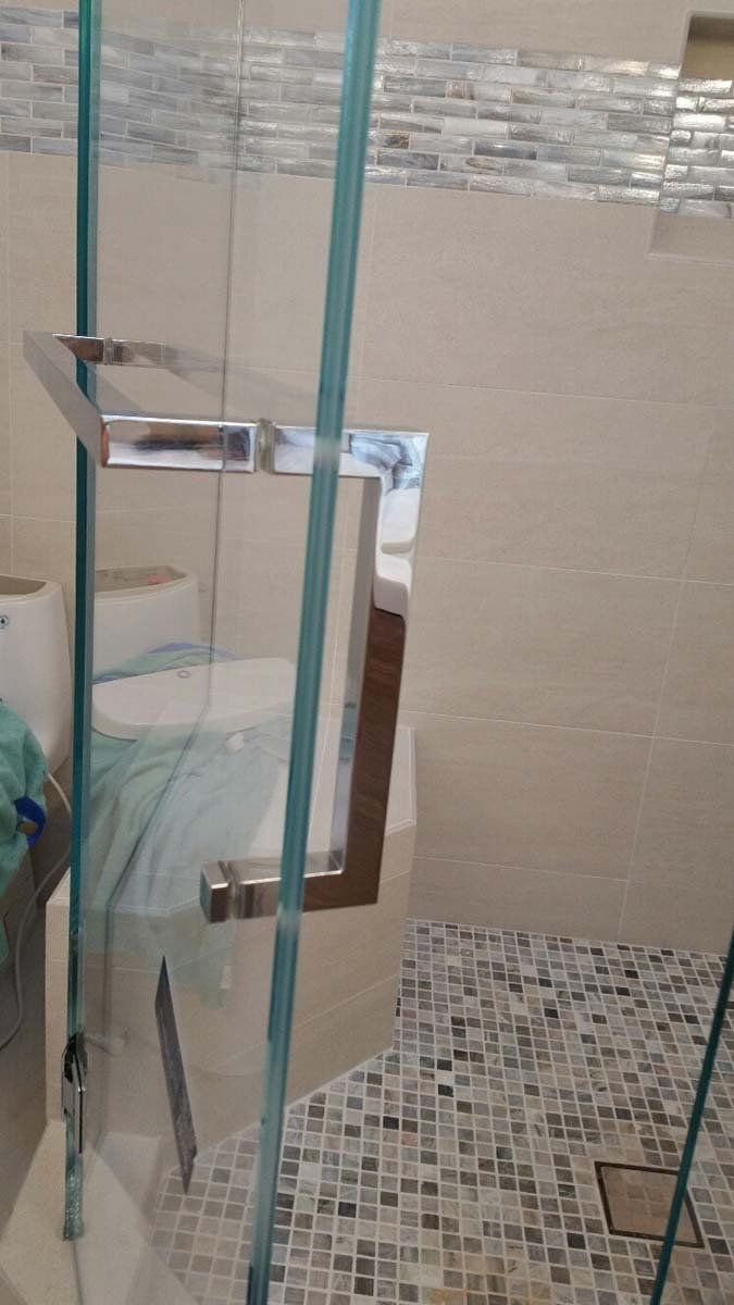 Glass shower door with chrome handle, beige tile walls, and mosaic floor.
