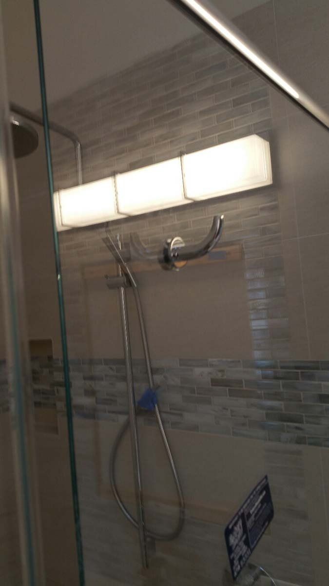 Shower interior with a light fixture, showerhead, and a hand shower. The tile features blues, and grays.