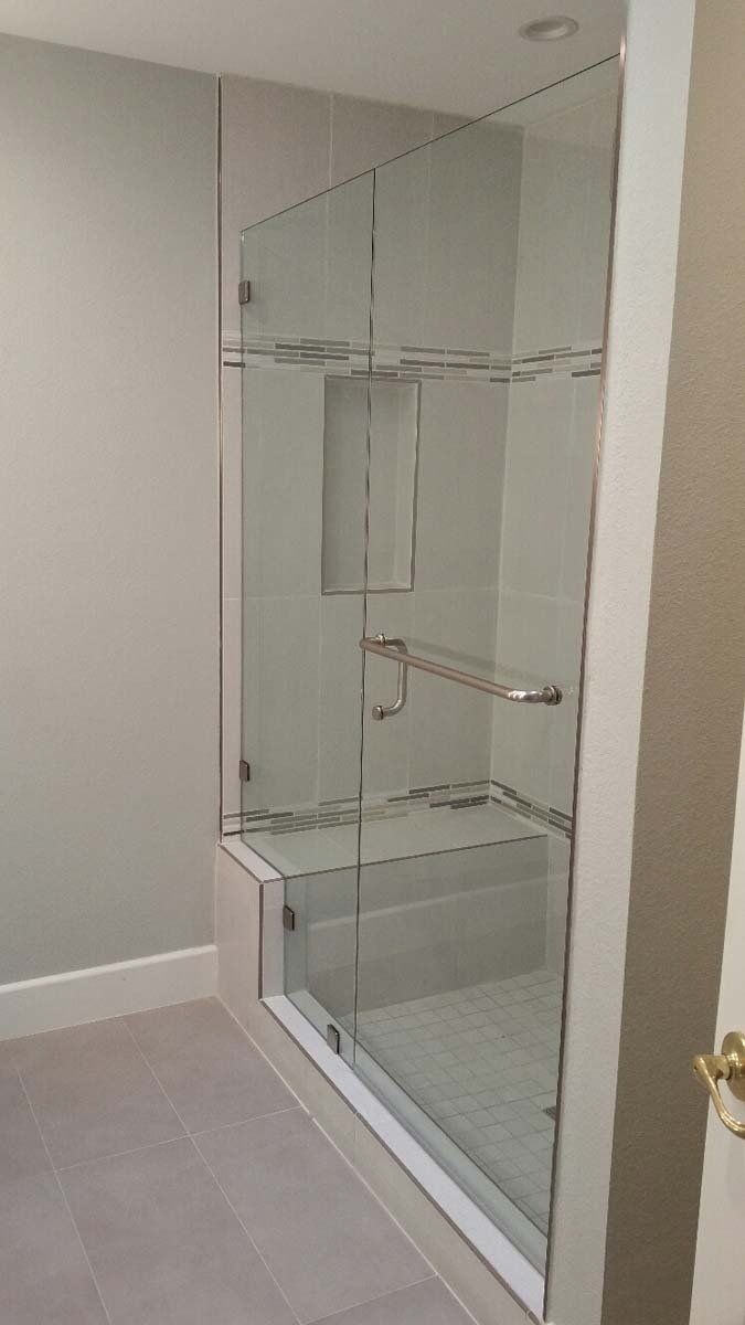 Glass shower with clear panels, chrome fixtures, built-in shelving, and a white tiled base in a bathroom.