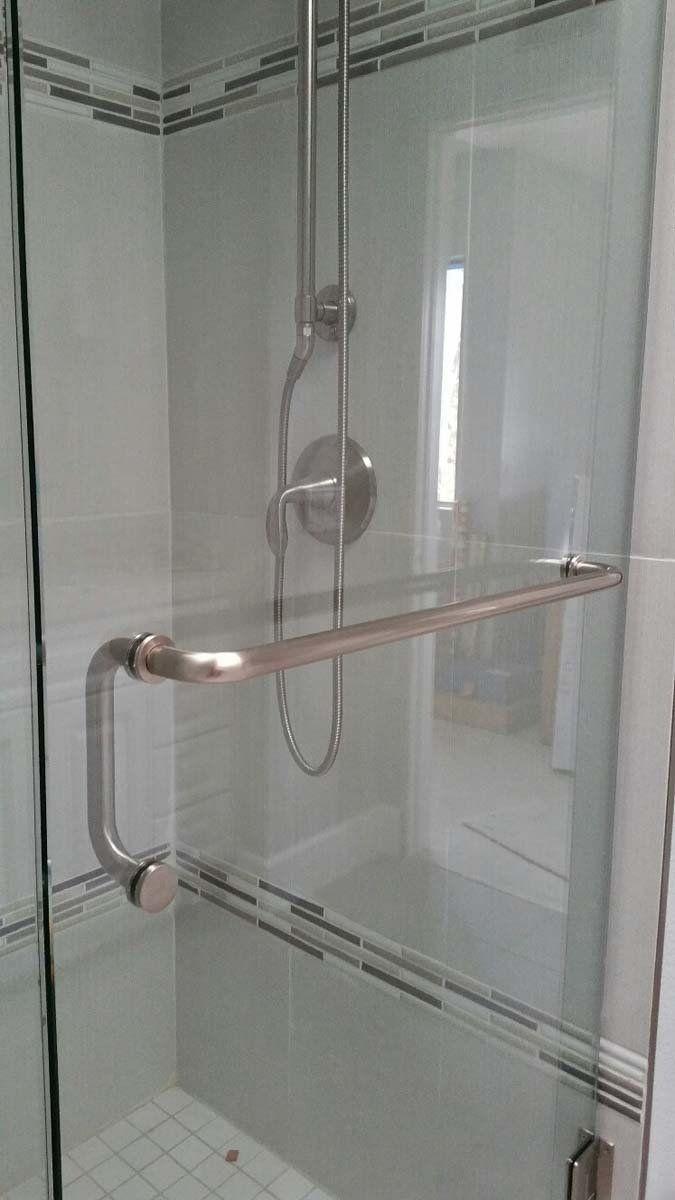 Glass shower door with chrome hardware, showerhead, and handle. White tile accents.