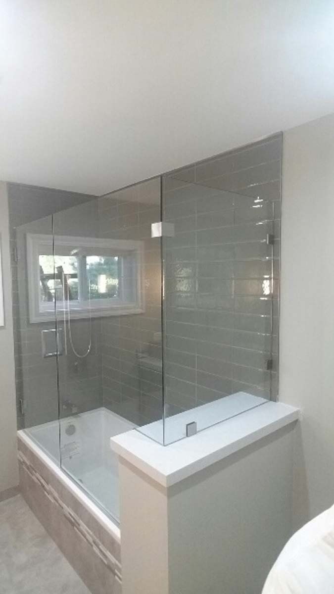 Glass shower enclosure with gray tile, a bathtub, and a window.