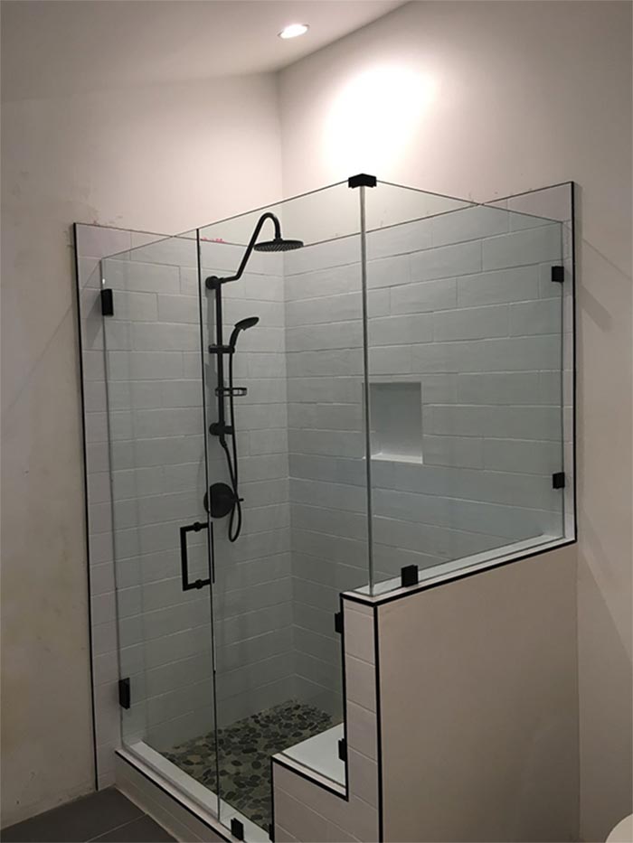 Glass shower with black fixtures and pebble floor, set in a white and gray tiled bathroom.