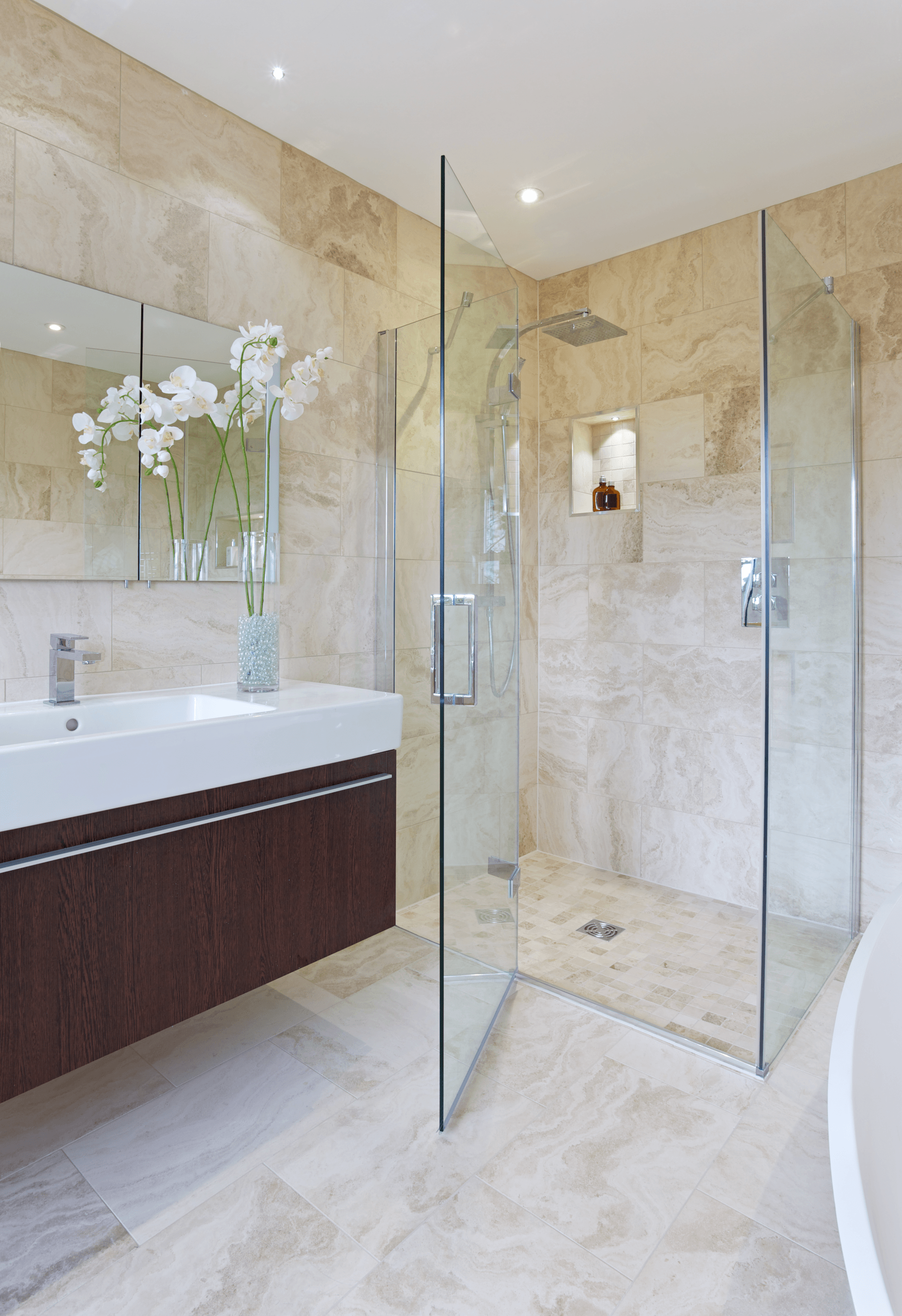 Modern bathroom with glass shower, vanity, and beige tiled walls.