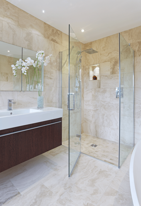 Elegant bathroom with a glass-enclosed shower, vanity, mirror, and beige stone tile.