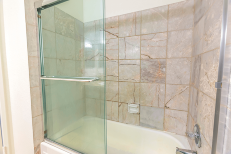 Shower stall with sliding glass doors, beige tile walls, and a white bathtub.