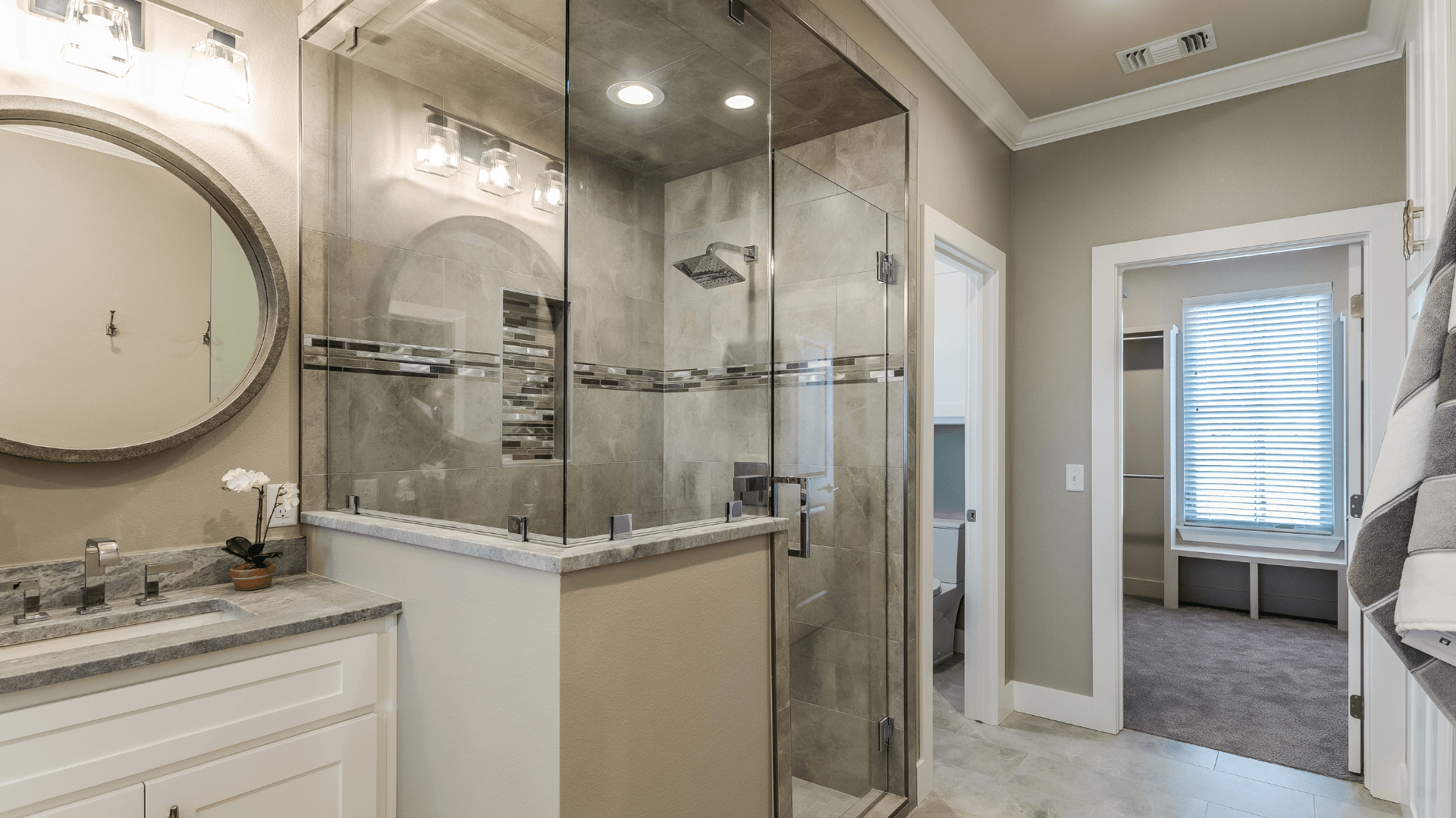 Modern bathroom with glass shower, vanity, and doorway to another room. Gray and white color scheme.