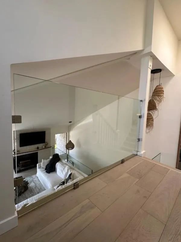 Modern home interior with glass stair railing, beige floor, and living room below