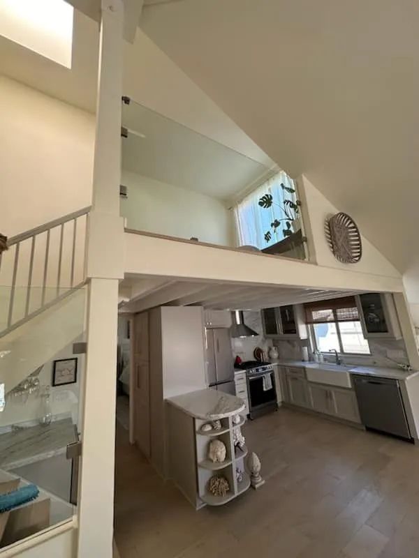 Bright, open living room with staircase, loft, and kitchen area in neutral tones