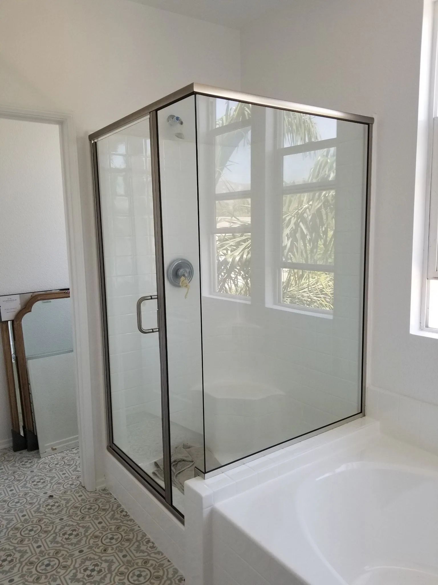 Glass corner shower enclosure beside a white bathtub in a bright bathroom