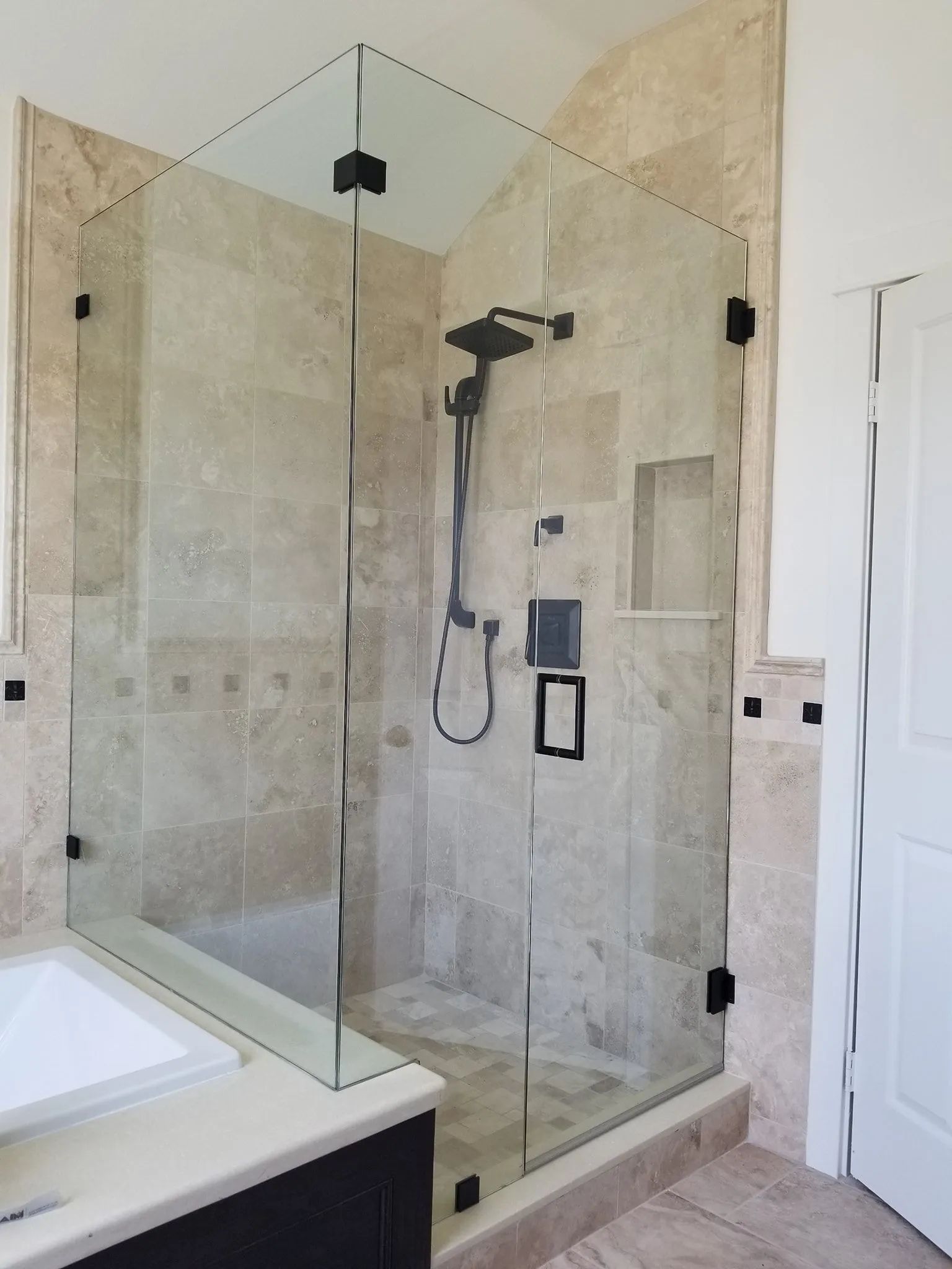 Walk-in tiled shower with glass enclosure, black fixtures, and white vanity in a bathroom