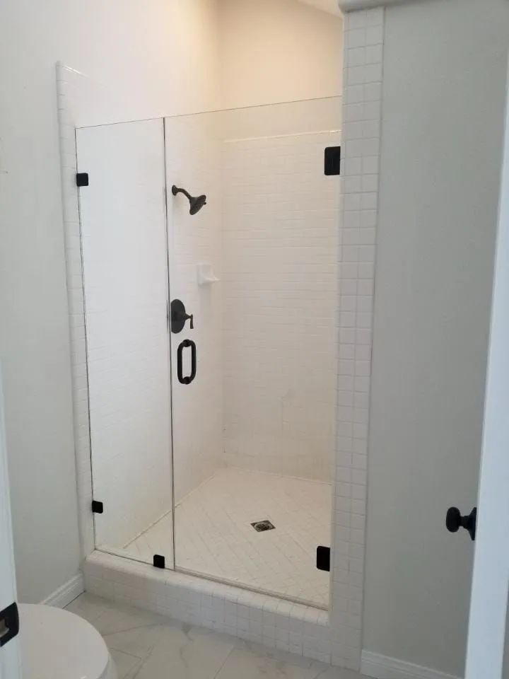 White tiled shower with glass door and black handles in a bathroom