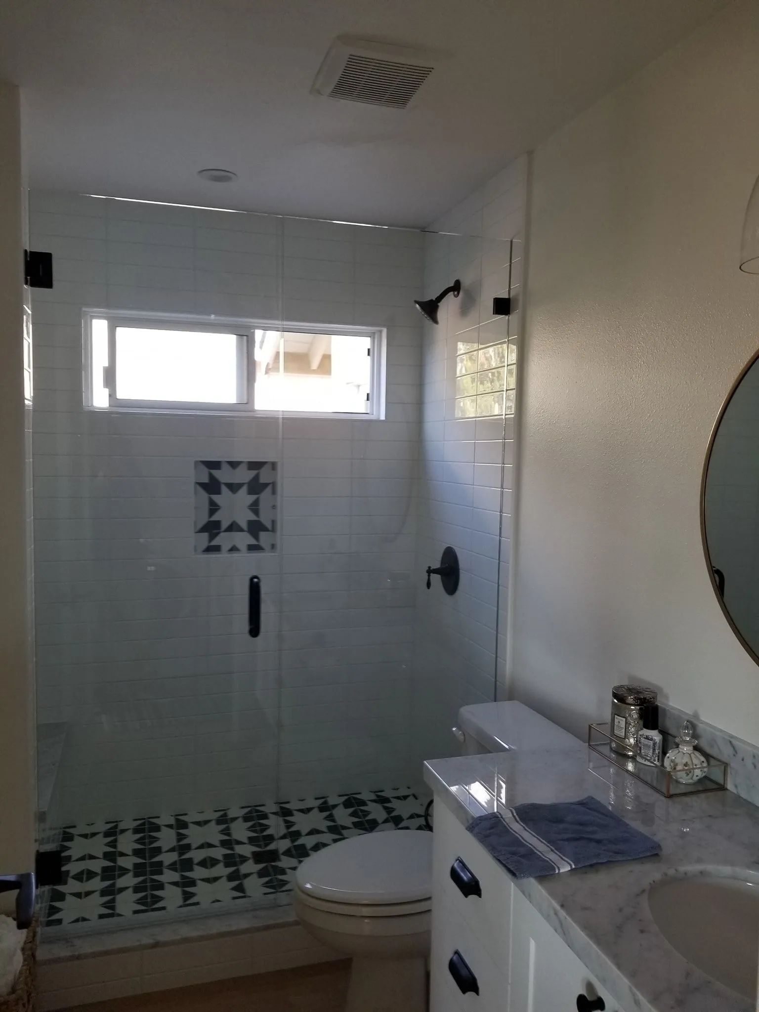 Small bathroom with tiled shower, toilet, vanity, and mirror in white and gray.