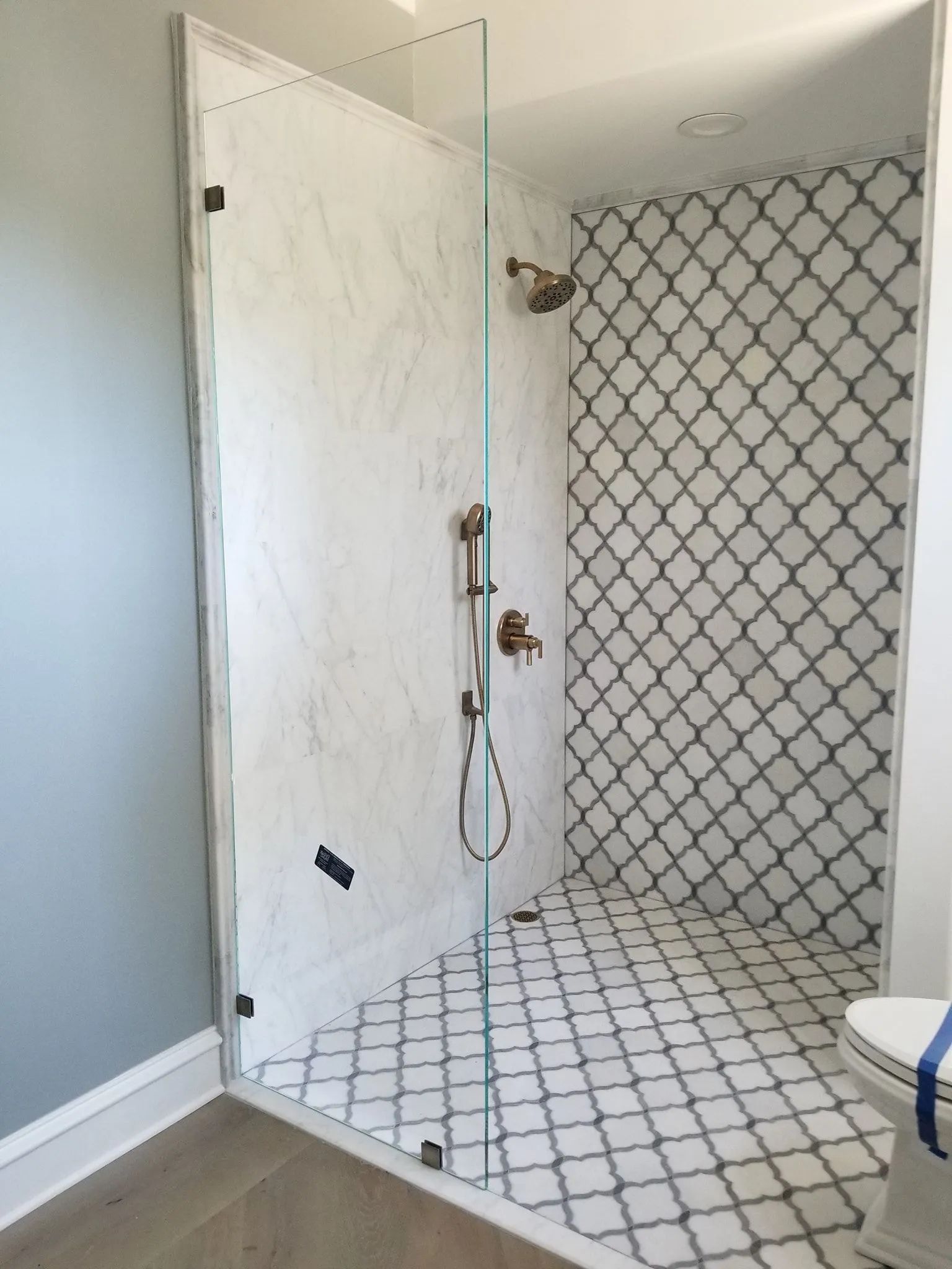 Walk-in shower with white tile and black diamond pattern, open door, and built-in showerhead.